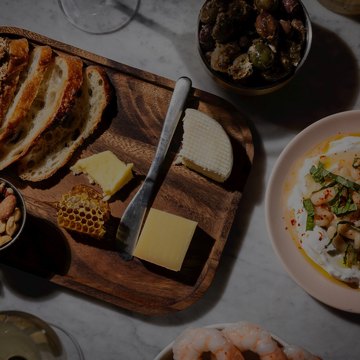 A wooden board of sliced bread, cheese and honeycomb, with bowls of olives, white beans and shrimp, on a marble table at Birds.