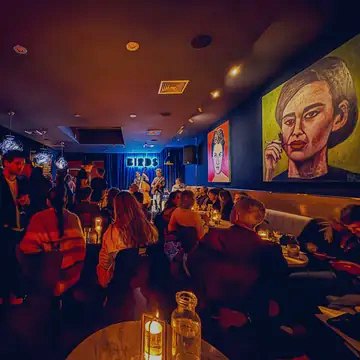 Guests seated at candlelit tables watching a trio play under the glowing Birds sign.