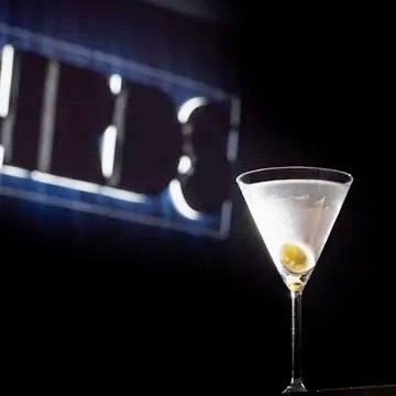 A martini with an olive in front of the softly glowing Birds sign.