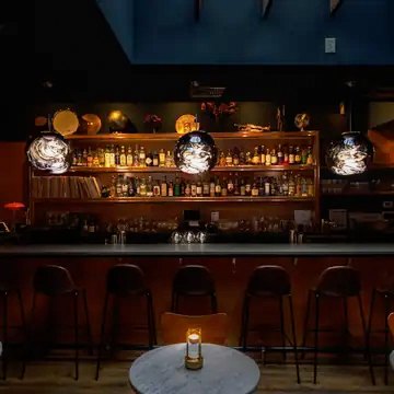 The bar at Birds, with a lit back bar, three glass pendant lights and a candlelit marble table in front.